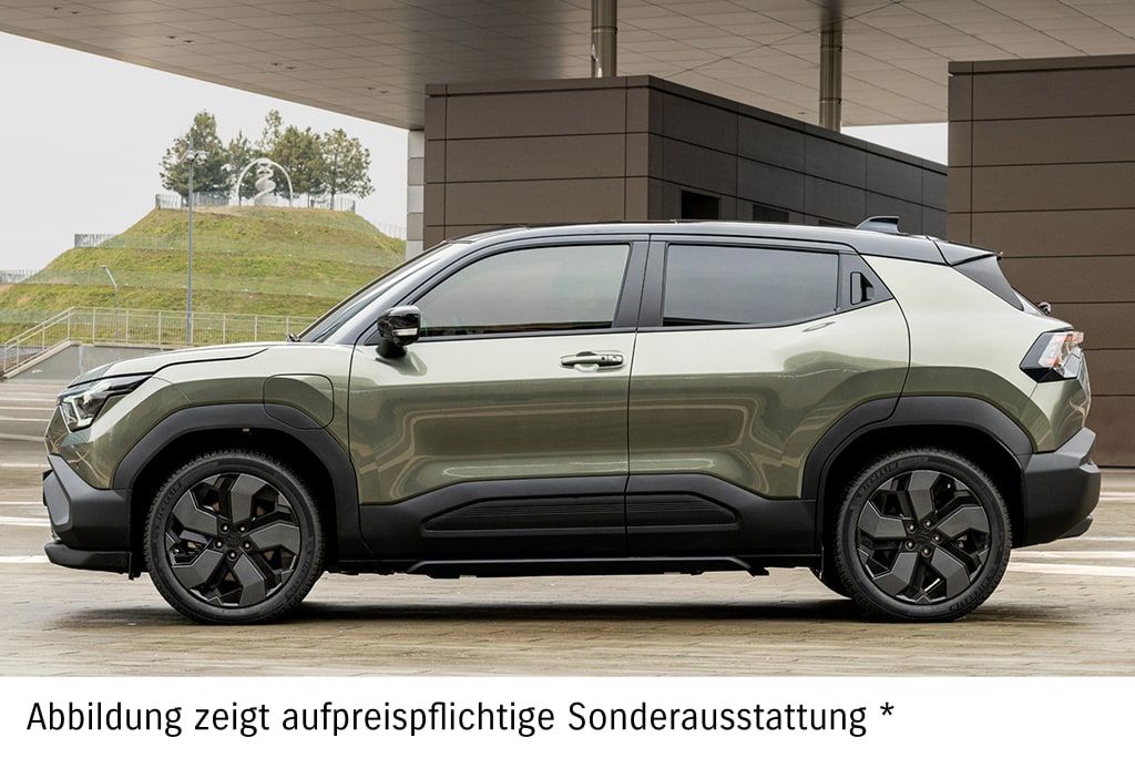 Grüner Suzuki e Vitara in Seitenansicht vor einer Hauswand.