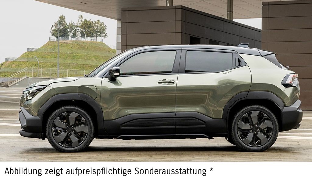 Grüner Suzuki e Vitara in Seitenansicht vor einer Hauswand.