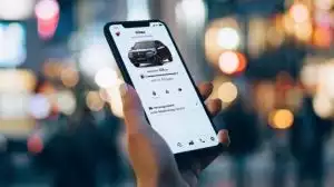 Nahaufnahme einer Hand, die ein Smartphone hält, auf dem die Suzuki CONNECT App genutzt wird vor verschwommenem City-Setting