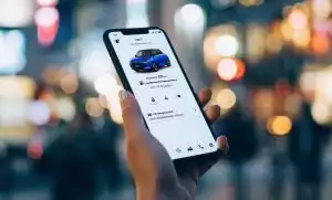 Nahaufnahme einer Hand, die ein Smartphone hält, auf dem die Suzuki CONNECT App genutzt wird vor verschwommenem City-Setting