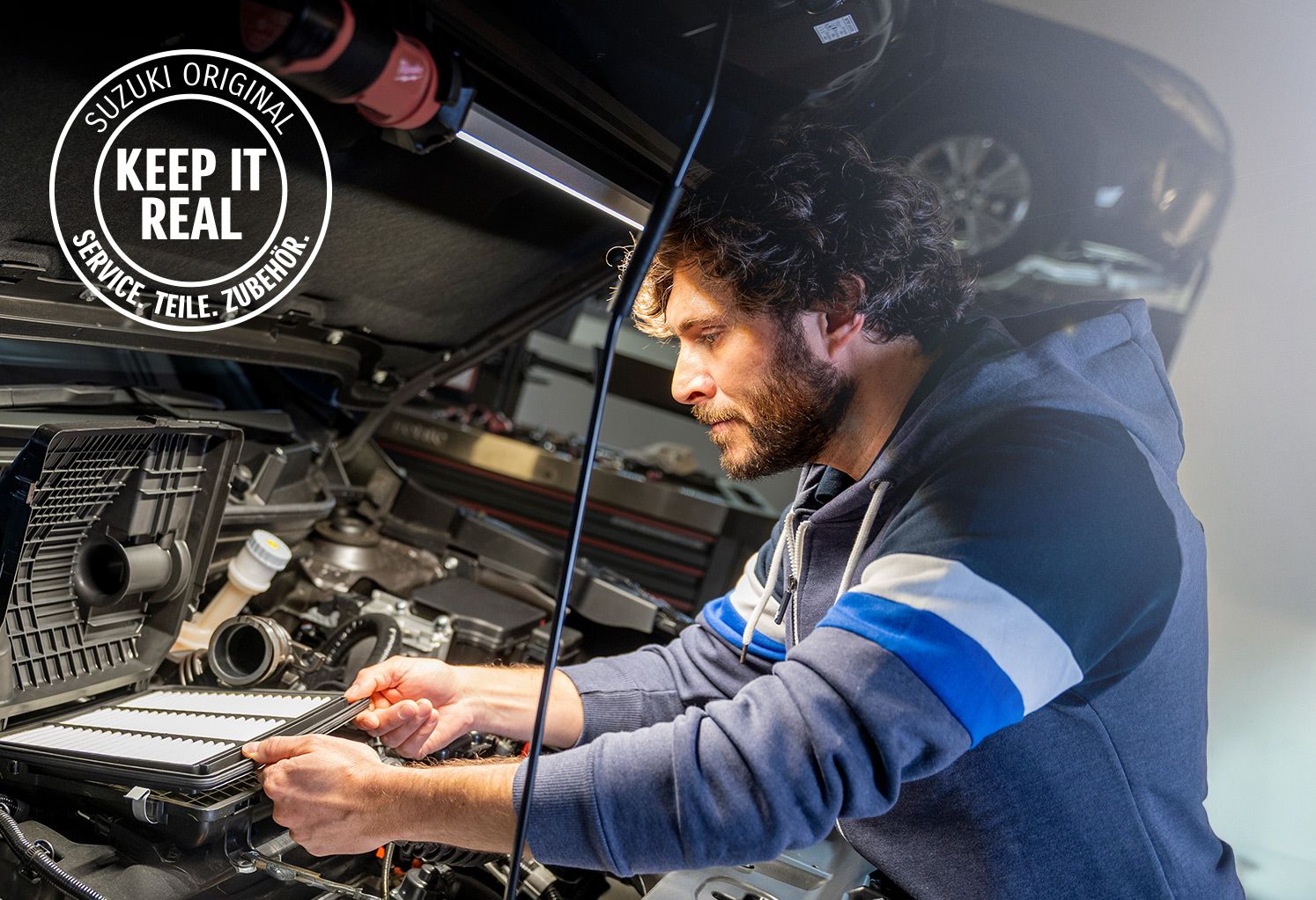 Mechaniker überprüft Luftfilter mit Suzuki „Keep it Real“-Logo.