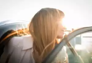 Seitenansicht einer jungen Frau, die bei Sonnenlicht lächelnd aus einem Auto steigt
