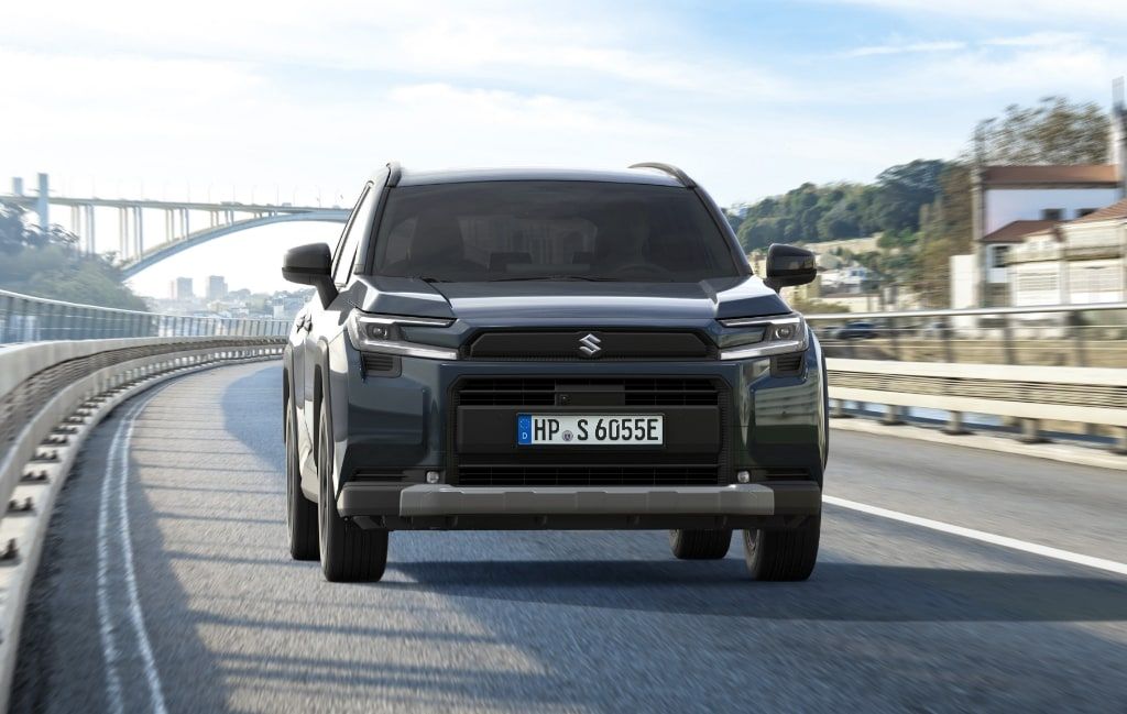 Weißer Suzuki Across PLUG-IN HYBRID Comfort+ bei Fahrt über Brücke in Front-Seitenansicht, Verbrauch 17,1 kWh/100 km, CO₂ 22 g/km, 6,6 l/100 km bei leerer Batterie