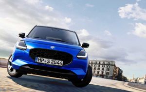 Blauer Suzuki Swift 1.2 DUALJET HYBRID Comfort+ von schräg unten vor City-Setting auf Kopfsteinpflaster