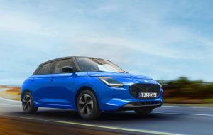 Blauer Suzuki Swift 1.2 DUALJET HYBRID Comfort+ auf einer Küstenstraße in Front-Seitenansicht