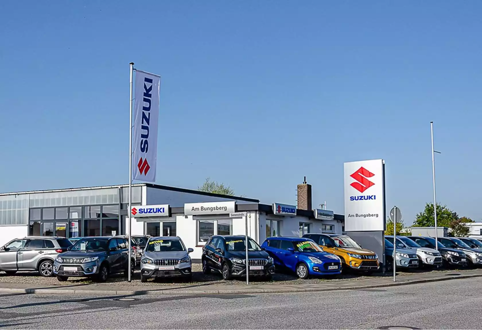 Blick auf das Suzuki Autohaus von der Straße aus mit Neufahrzeugen vor dem Gebäude